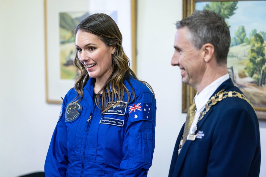 An astronaut in a flight suit standing next to a mayor.  