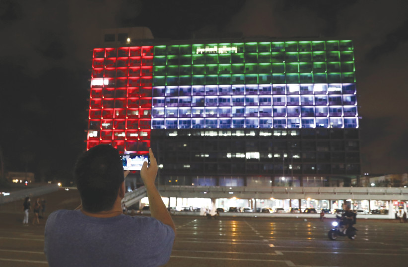A MAN takes a picture as Tel Aviv City Hall is lit in the image of the United Arab Emirates national flag, following the announcement of a deal to normalize relations.