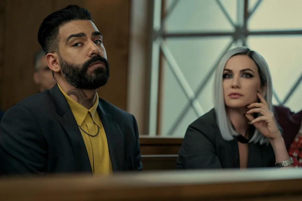 A man and woman in formal attire sit attentively in a courtroom setting