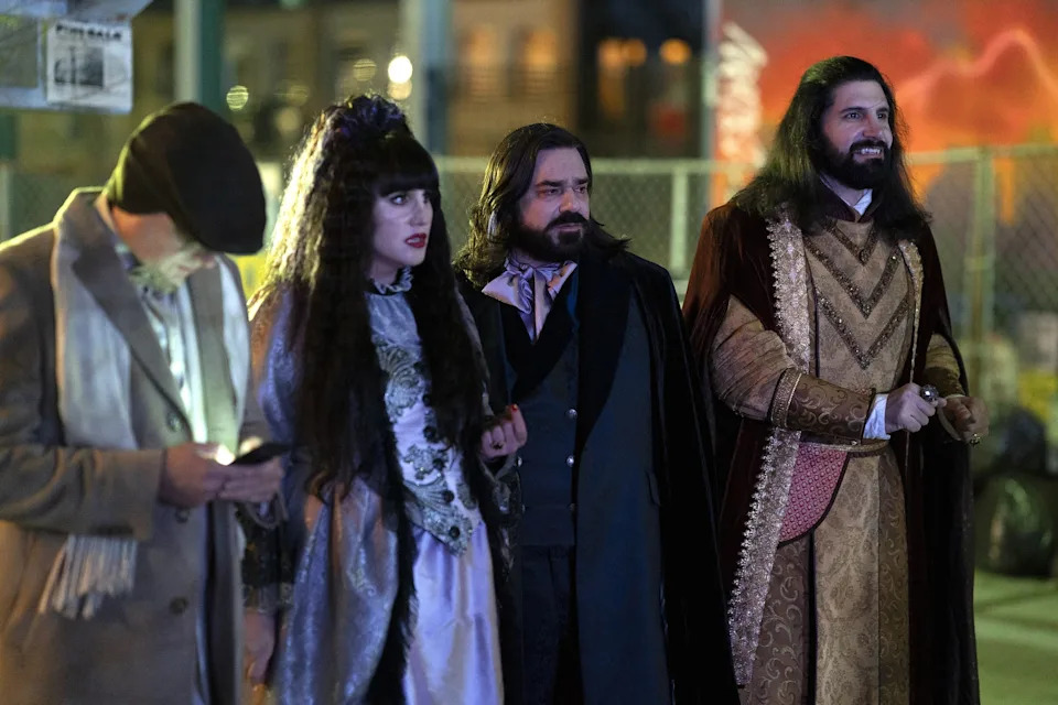 Four people in gothic and medieval-inspired outfits standing together at an outdoor event, with one person using a phone