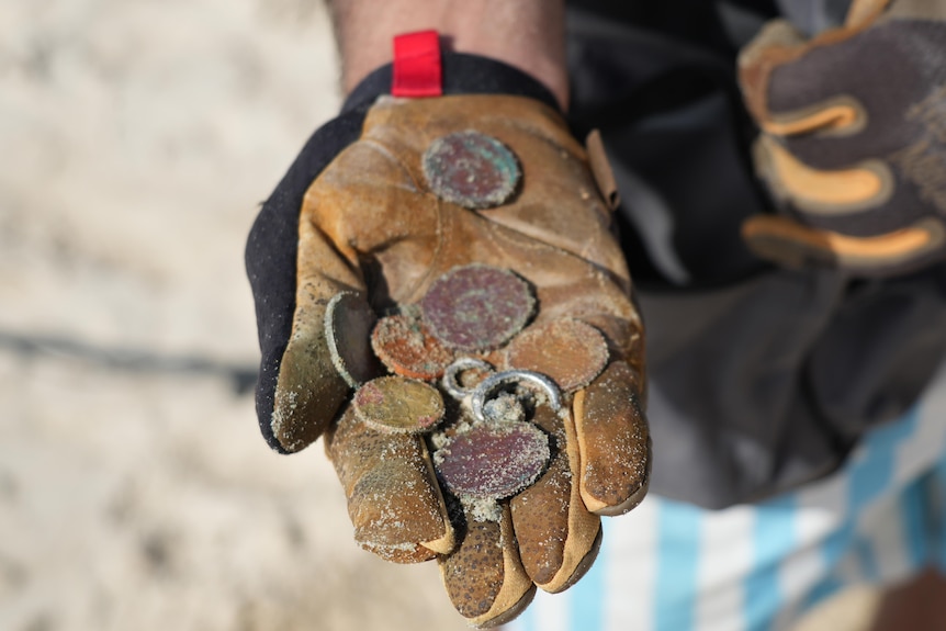 A gloved hand holds coins and a silver ring