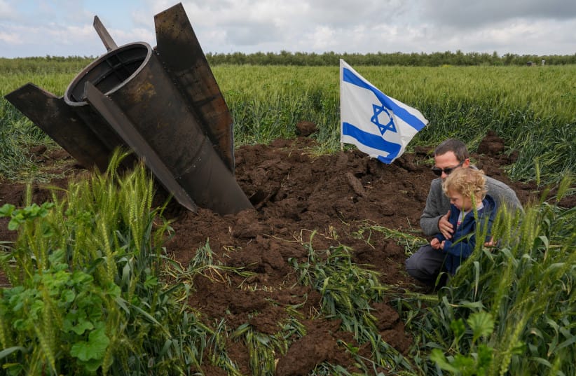 A man and his child next to a fragment of a missile fired from Iran toward Israel, intercepted by Israeli air defense systems, seen lodged in the ground in the Golan Heights, April 8, 2026.