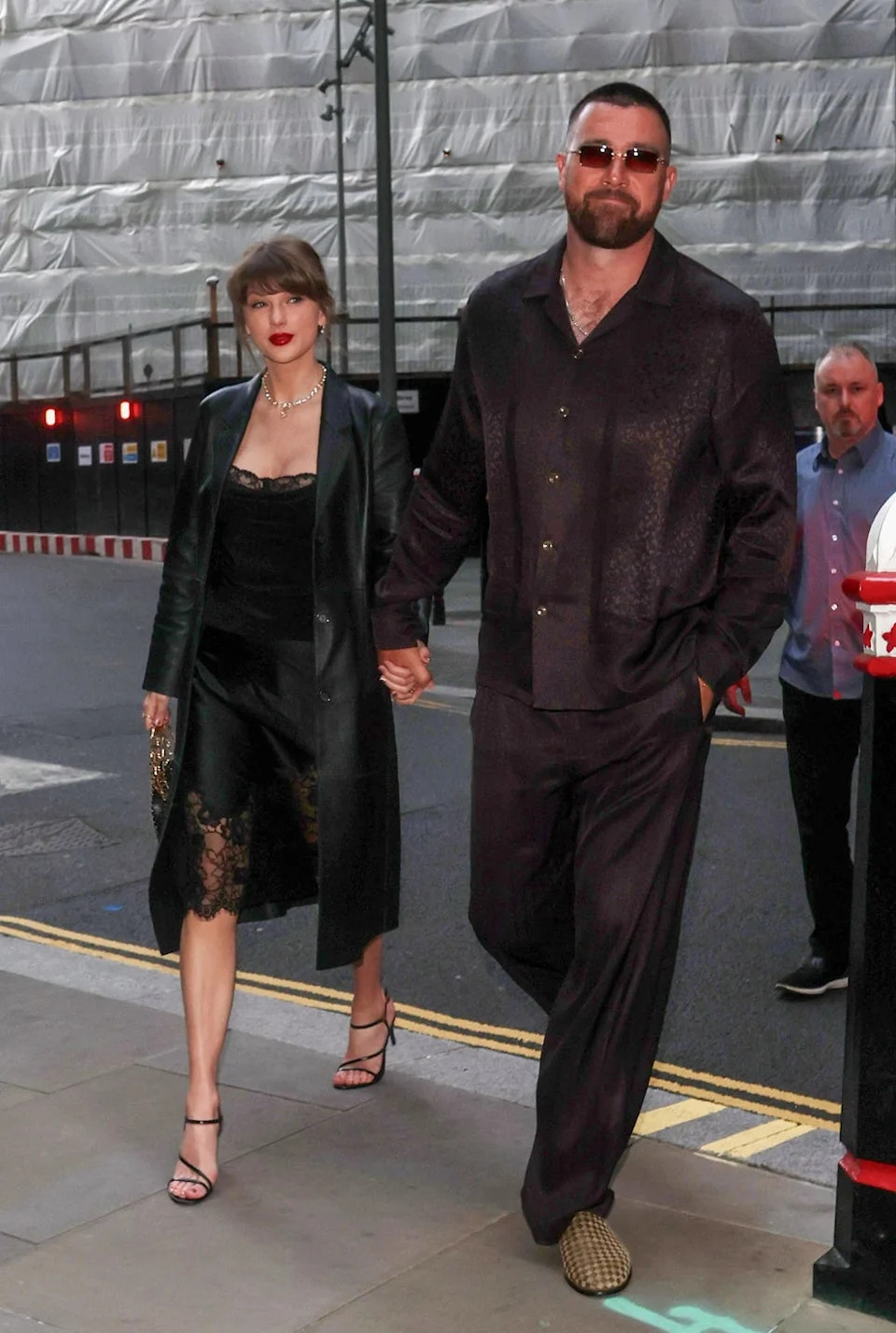 A couple walking hand in hand down a city street during the evening.