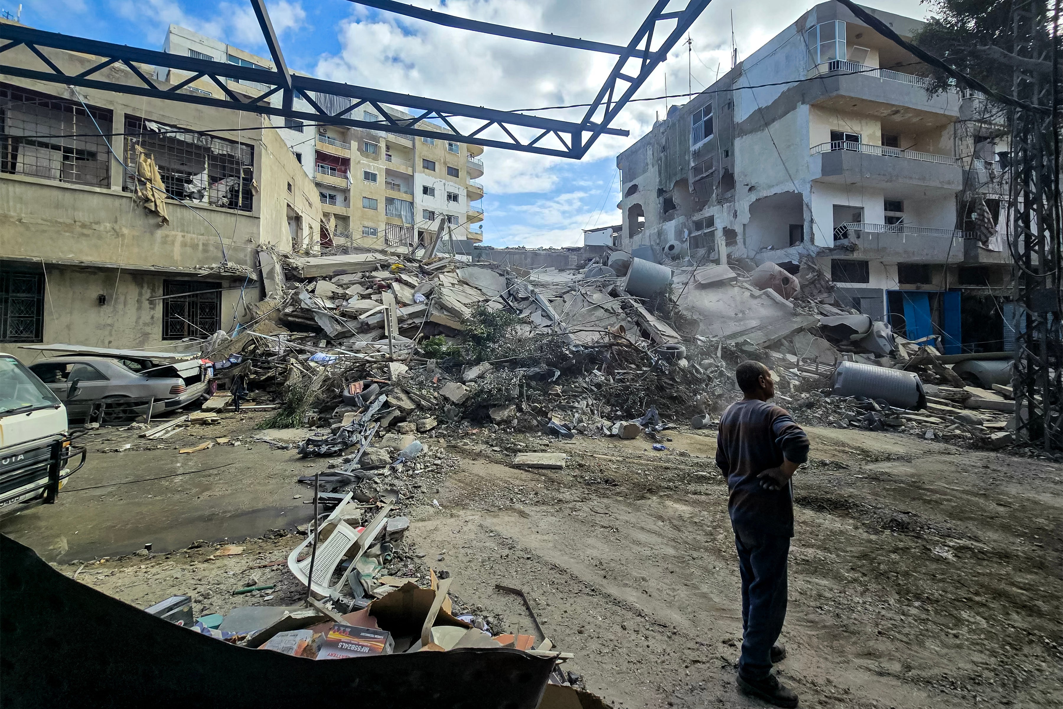 People stand by rubble and debris near damaged and collapsed buildings following overnight Israeli bombardment on Lebanon's southern city of Tyre on May 16, 2026