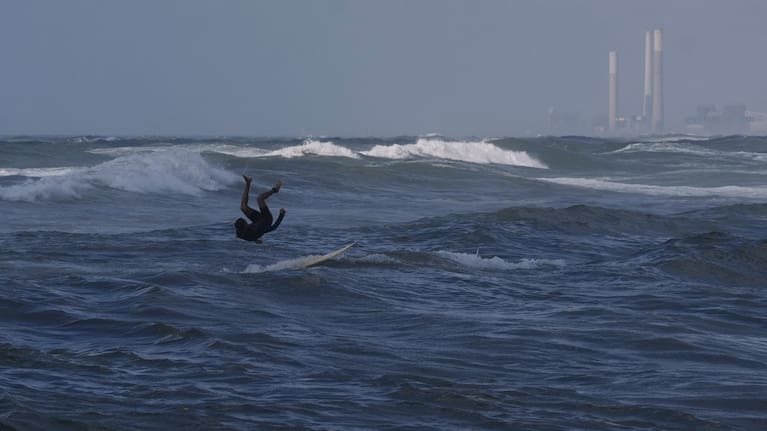 A Palestinian jumps into the waters of the Mediterranean Sea as he surfs on the beach in Gaza City, Monday, May 4, 2026.