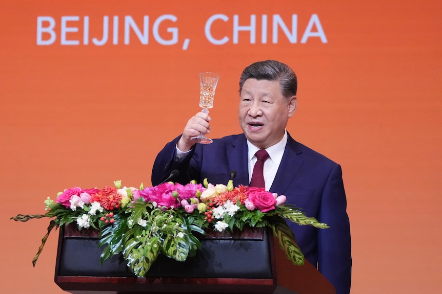 A man raises a glass of champagne from behind a lectern.