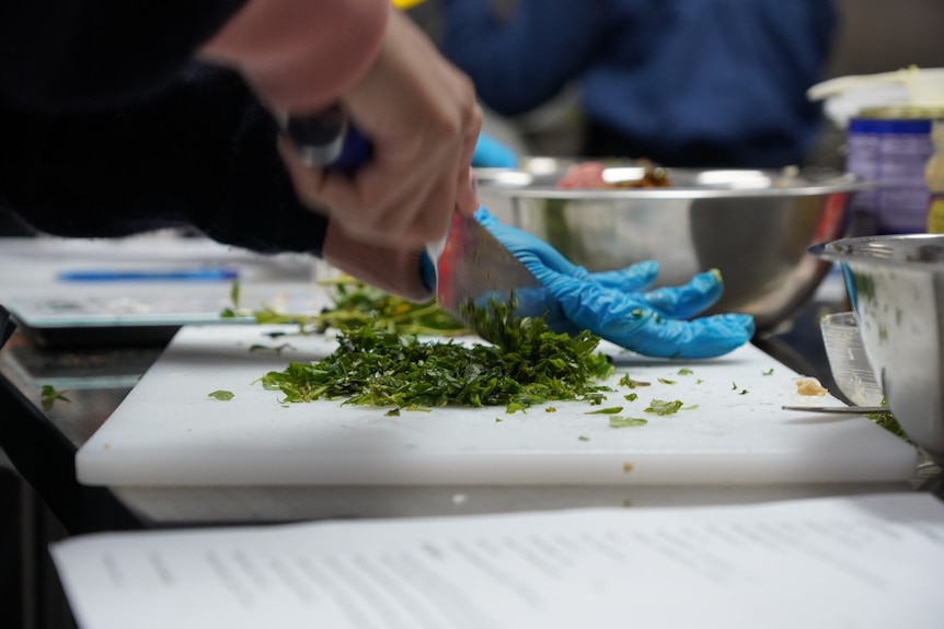 Close up of a hand holding a knife and chopping herbs