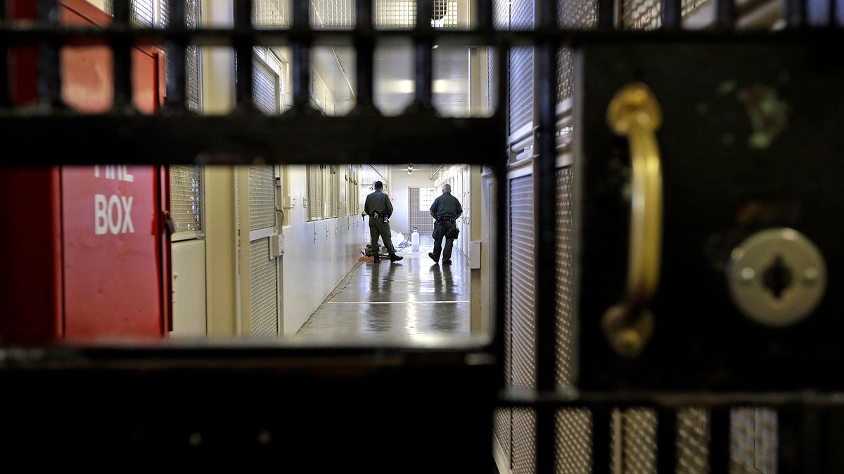 A photo shows the open slot of a prison gate, where two prison guards are standing in the middle of a corridor.