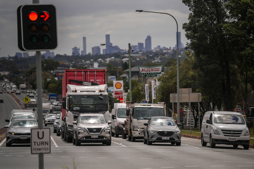 Traffic sitting at a set of red traffic lights on Beaudesert Road with Brisbane City skyscrapers in the background.