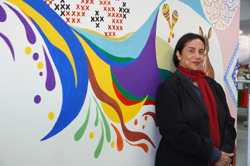 A woman smiles at the camera while standing in front of a mural