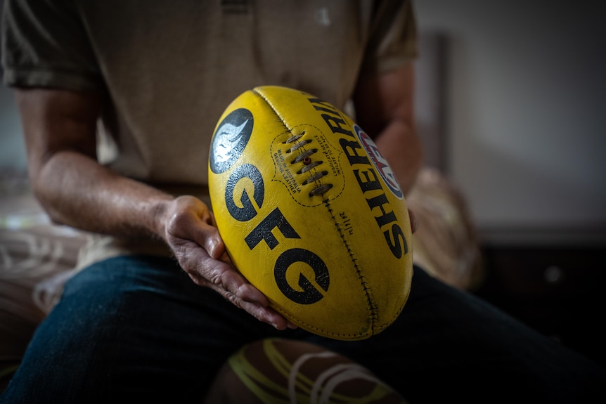 An Adelaide resident holding a football at his suburban home.