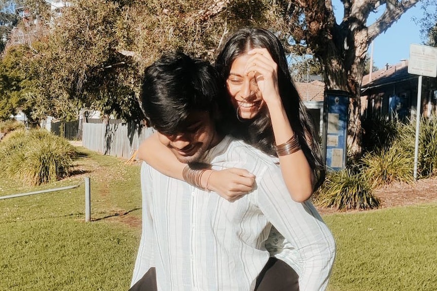 A young man in a garden gives a woman a piggyback while she smiles