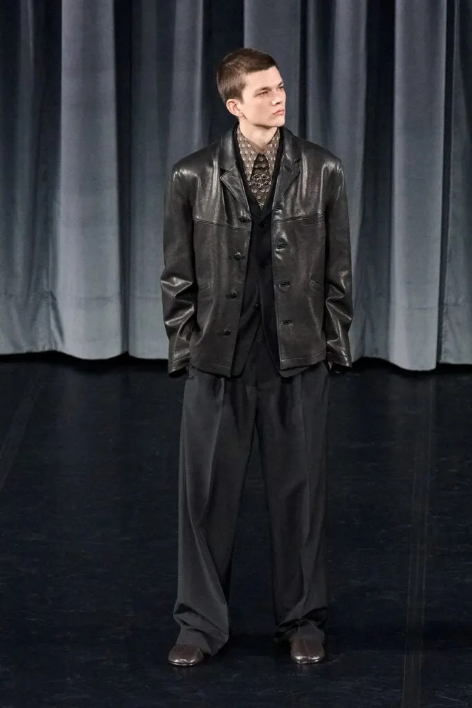Lemaire Fall 2026 menswear look featuring a patterned shirt, knit vest and relaxed tailoring on the runway.