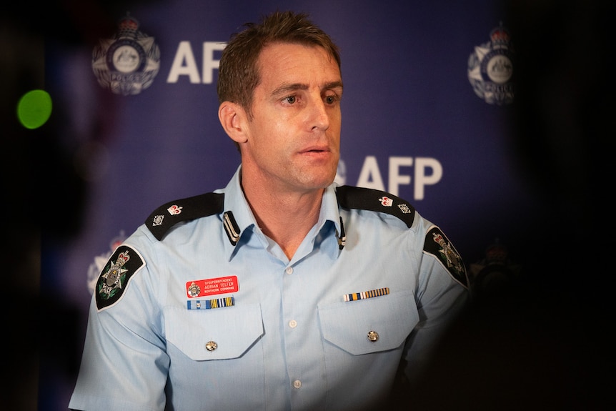 Male federal police office talking to media with AFP banner in background