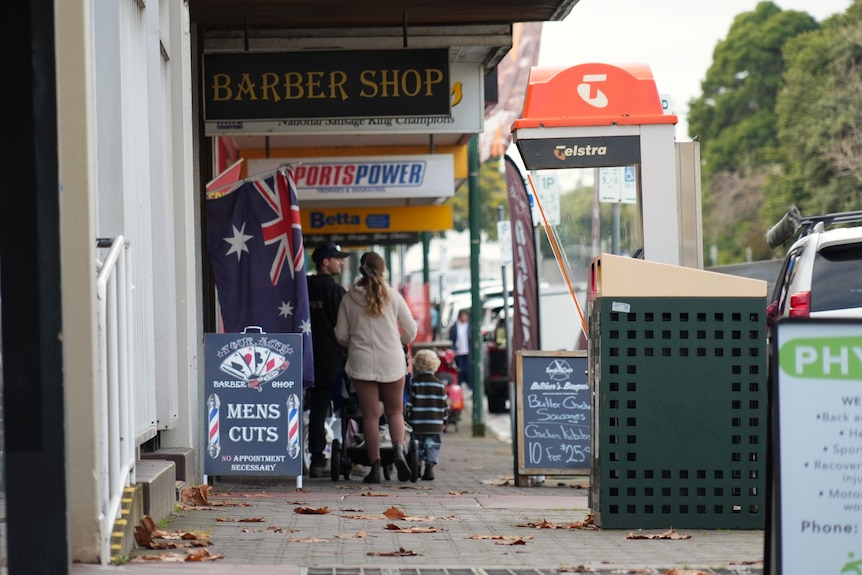 A grey footpath alongside a road with colourful signs of different businesses hanging from the roof and people walking by.