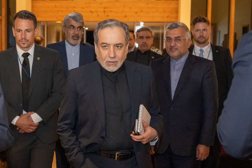 Seyyed Abbas Araghchi walks, looking serious, surrounded by men in suits.