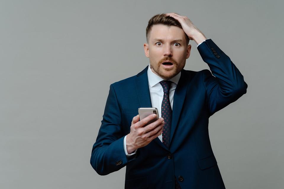 Shocked person in suit holding smartphone.