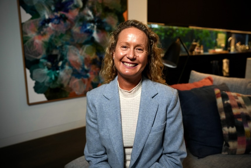 A middle-aged woman in a powder-blue jacket smiles at the camera.