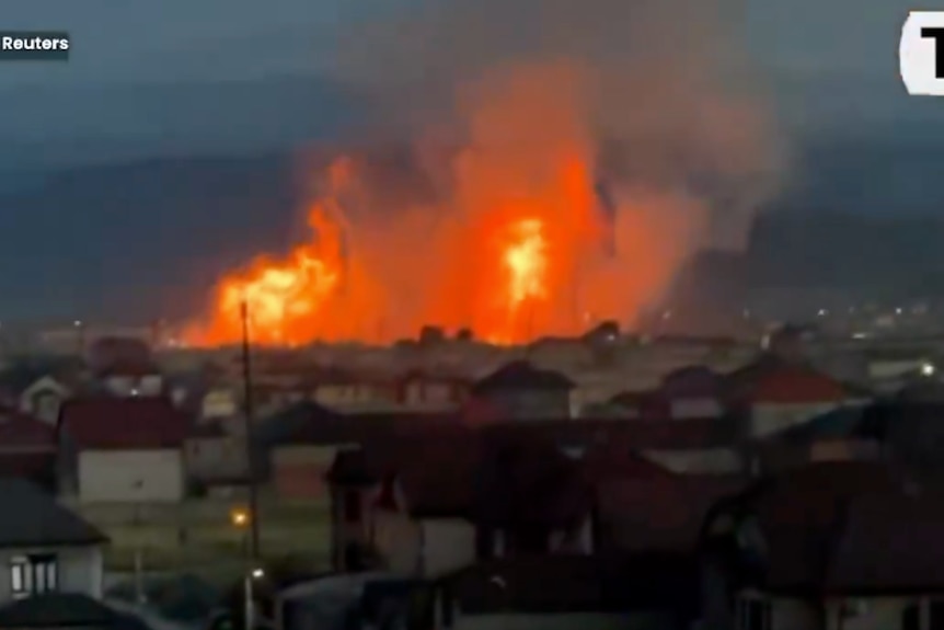 In the foreground, houses, in the background, a large set of flames.