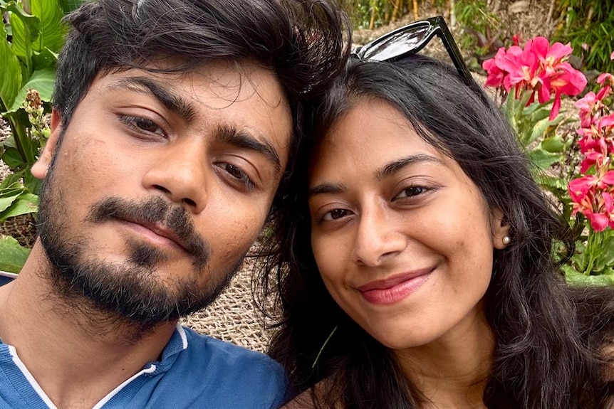 A young man and young woman in a garden smile at the camera