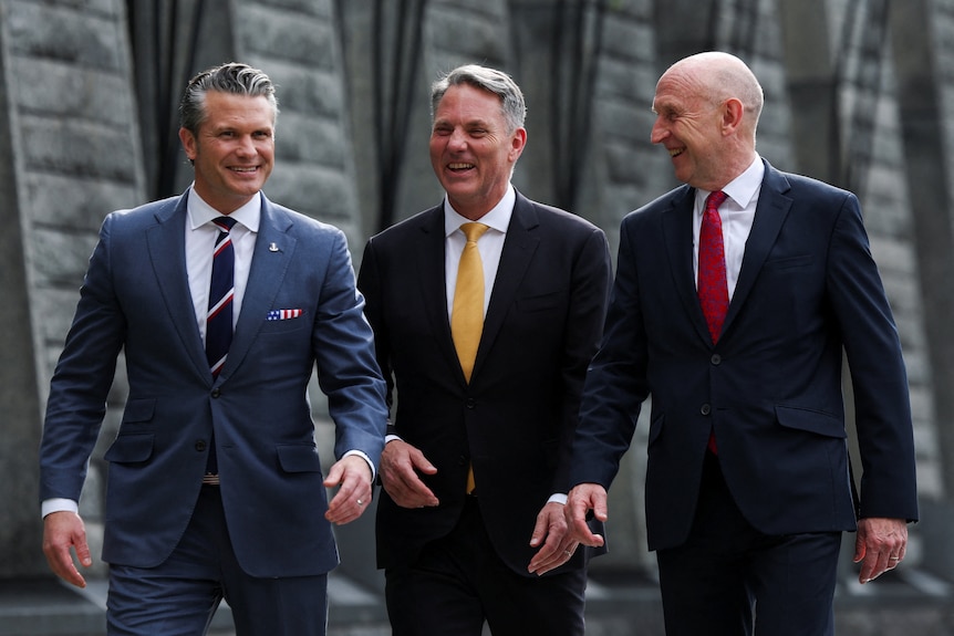 Three men in suits and ties walk together outside with happy expressions