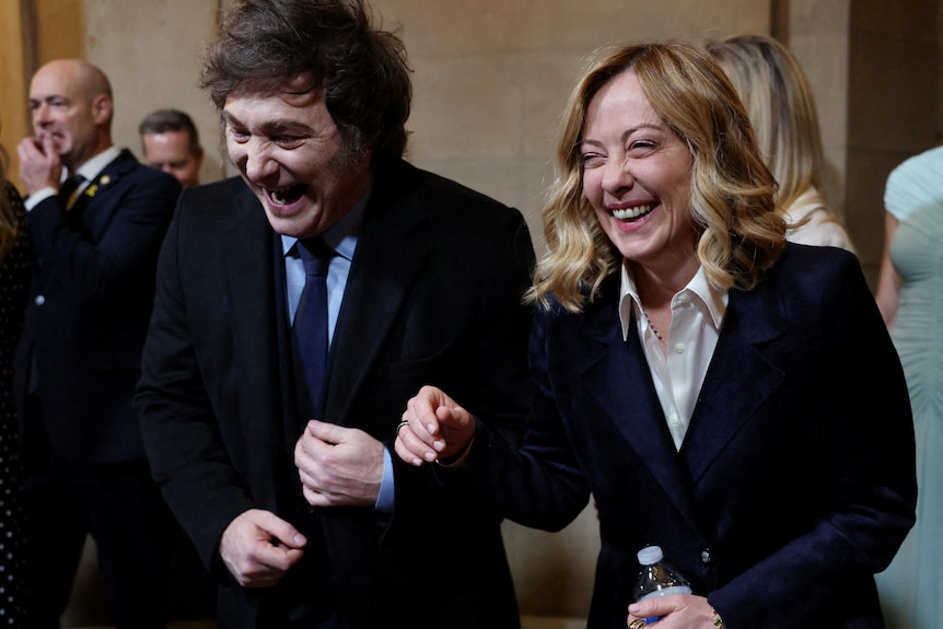 A man with huge sideburns and a woman with blonde hair laugh heartily together