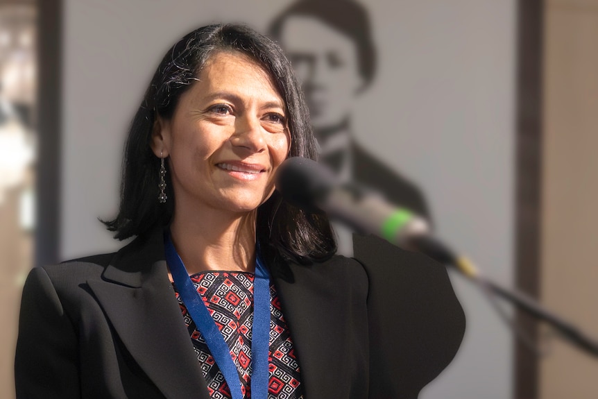 A woman smiles while giving an address at a podium.