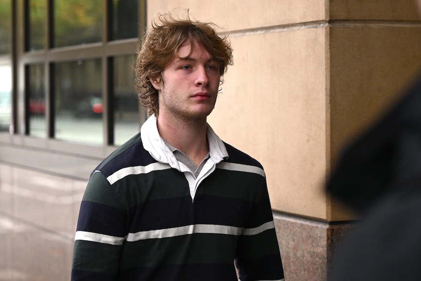 A man in a collared rugby jumper walks outside court.