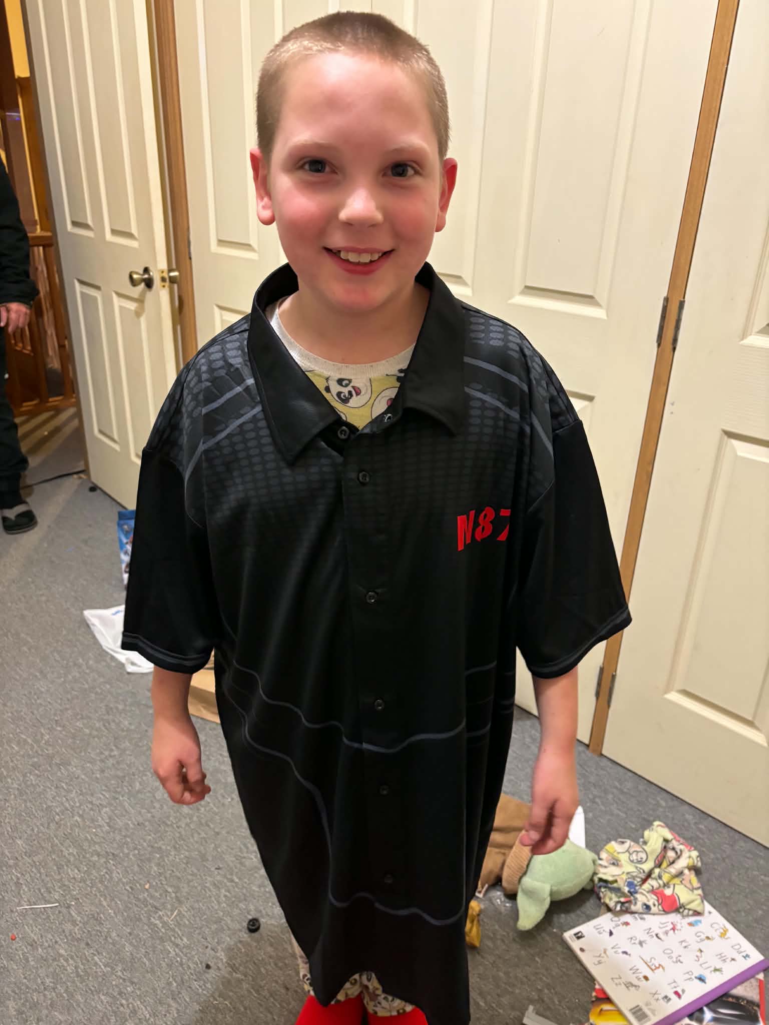 A smiling boy in a ddark shirt stands in a house.