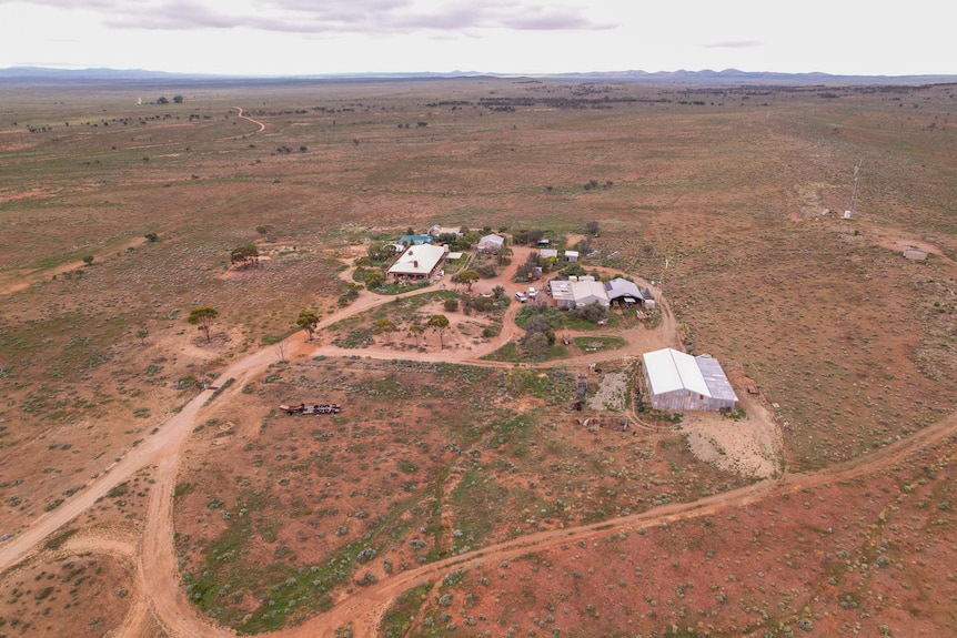 Farm buildings and a house in a brown landscape with low hills taken from a drone