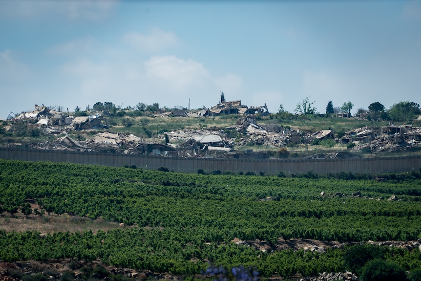 Destroyed buildings litter the ground above green fields.