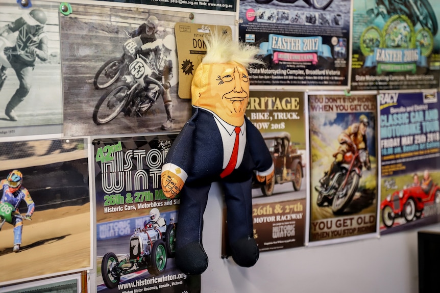 A soft toy doll of Donald Trump pinned to a shop wall with posters behind it.