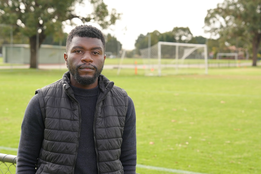 A man wears black clothing and stands in front of a soccer goal on a field.