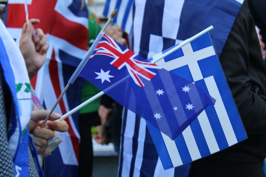 Hands wave small Greek and Australian flags.