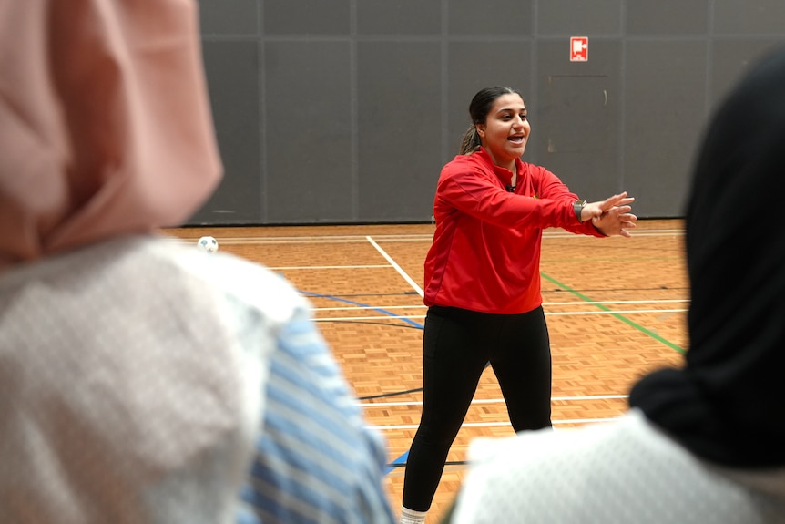 A woman wears a red jumper while coaching on an indoor court.