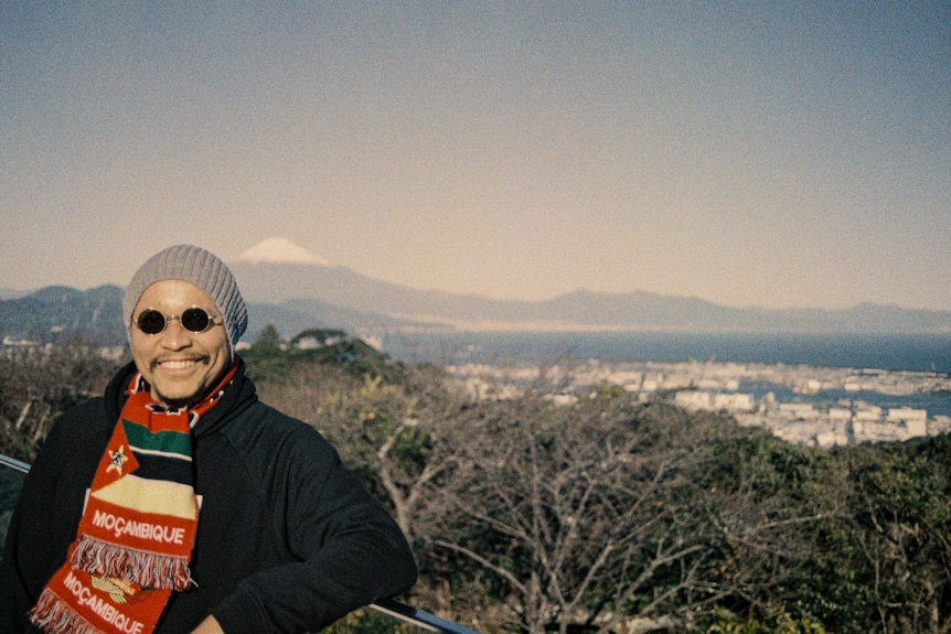 Miguel Carmichael, wearing a beanie, sunglasses and Mozambique scarf in front of Mt Fuji.