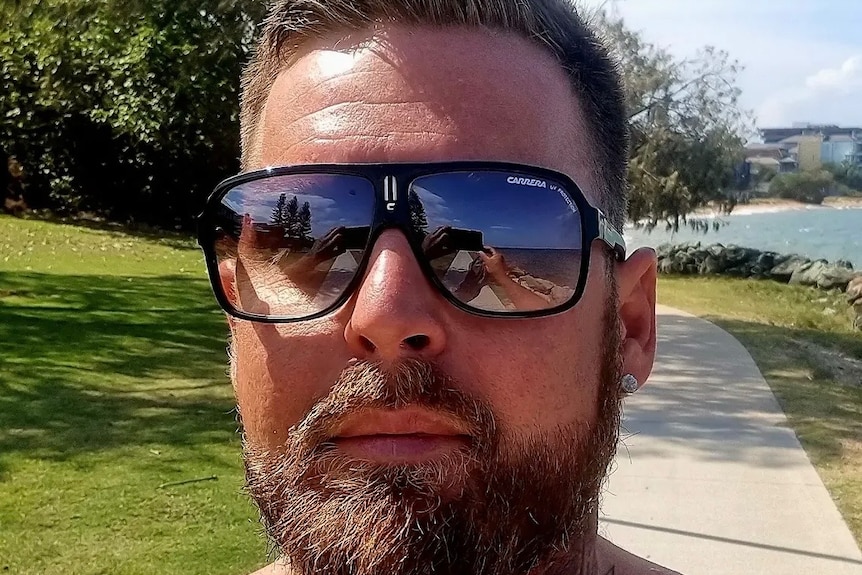 A shirtless man with beard and sunglasses takes a selfie