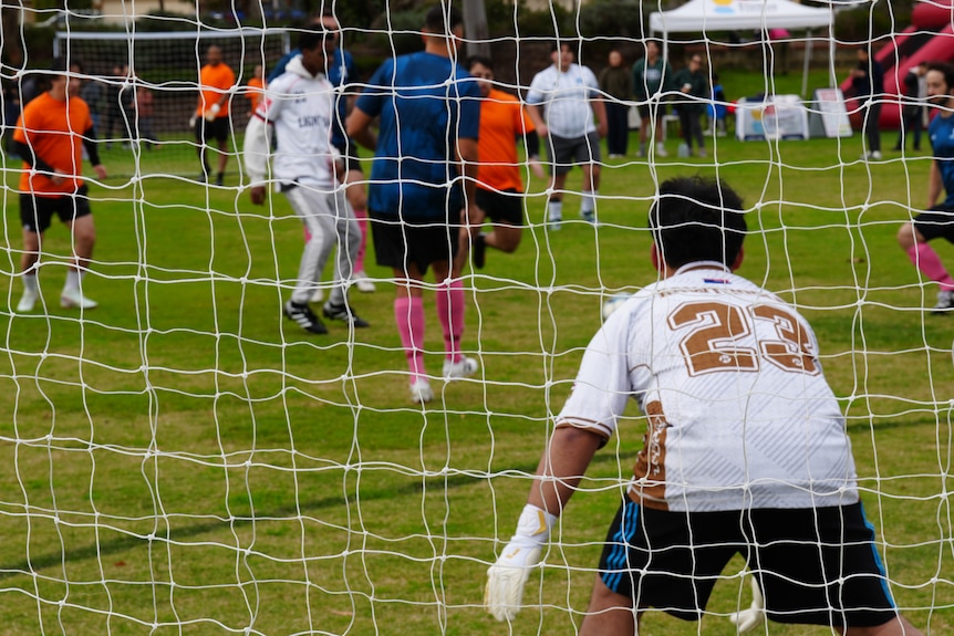 A goalie stands with his back to the camera during a soccer game.