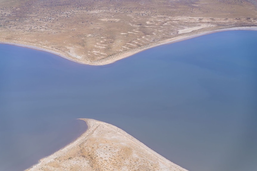 An hourglass shaped shoreline with sand top and bottom of the photo, and water through the middle, taken from the sky