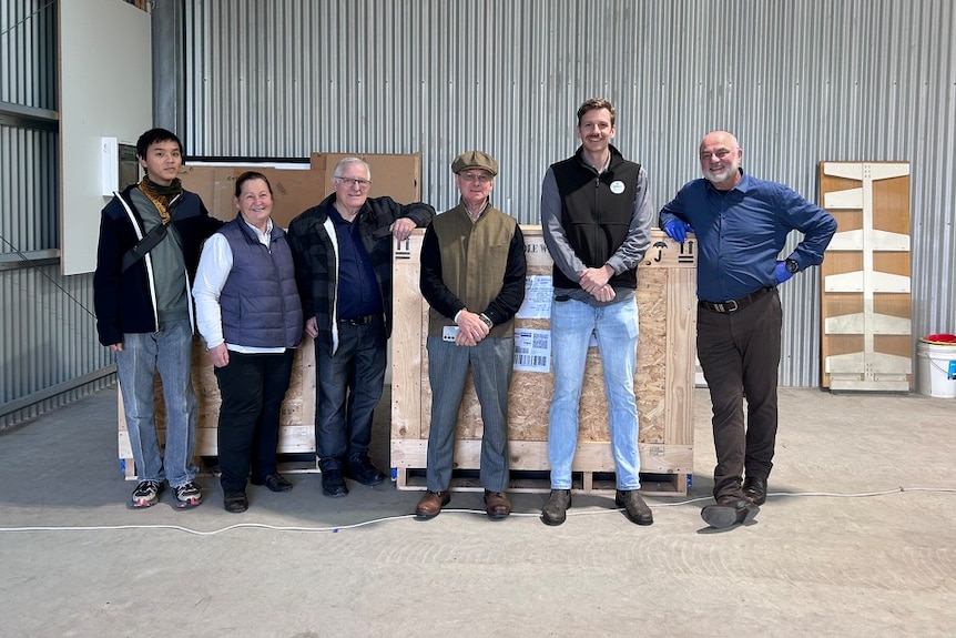 Six people standing in a warehouse in front of two large wooden crates.