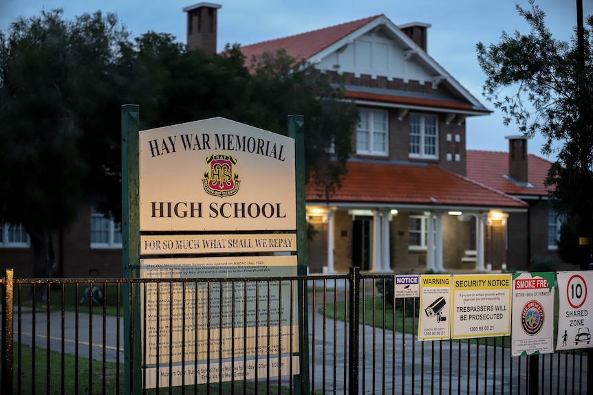 A historic red brick building with a sign in front reading 'Hay War Memorial High School'