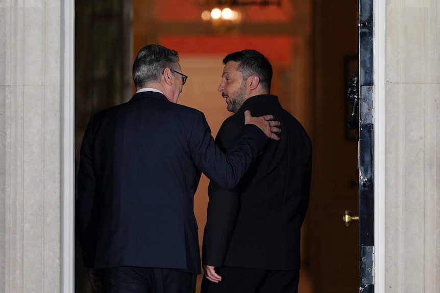 Sir Keir Starmer has his hand on Volodymyr Zelenskyy's shoulder as they walk through a door.