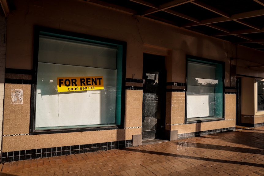 A vacant shop window with a yellow Rent sticker on a country street at sunrise