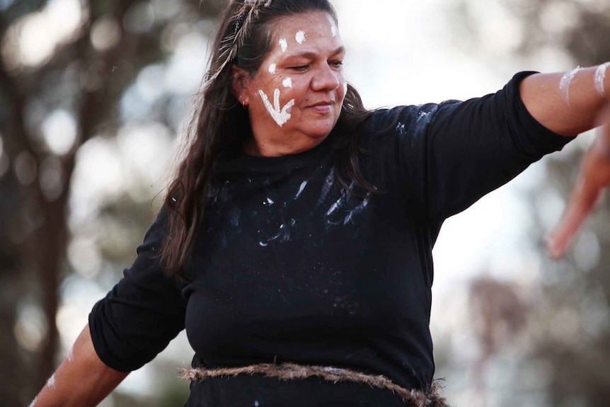 A dancing middle-aged woman with traditional paint on her face and clothes.