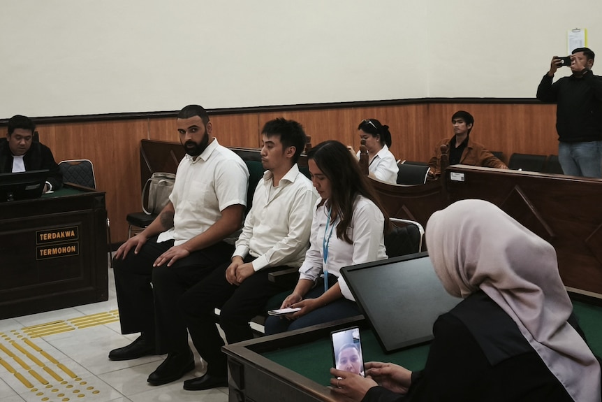 Two men and a woman sit in an Indonesian courtroom.