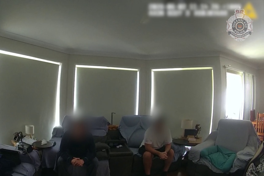 Two people with faces blurred sit on a couch indoors