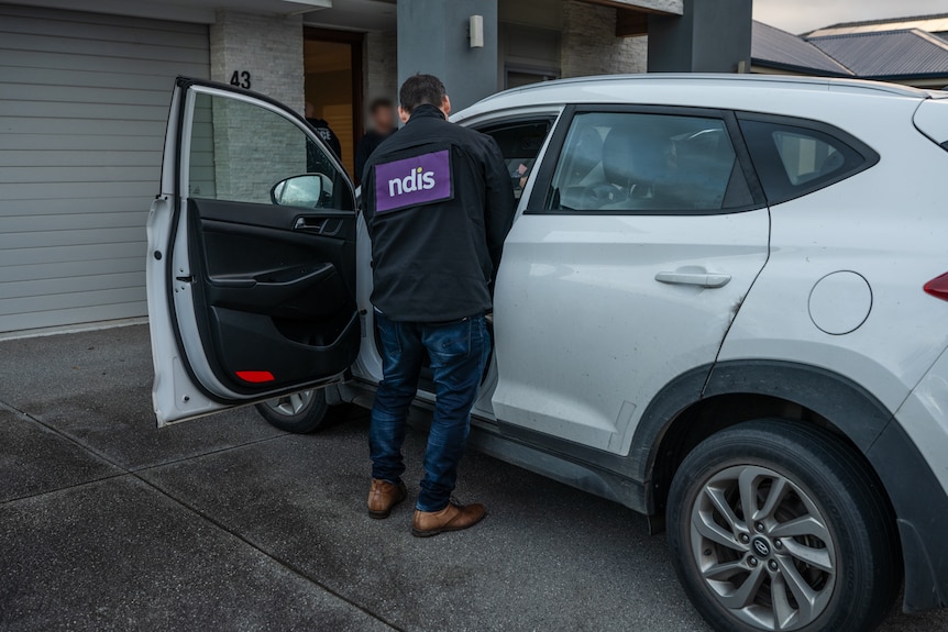 A person with NDIS on their back looks in a white small four-wheel drive