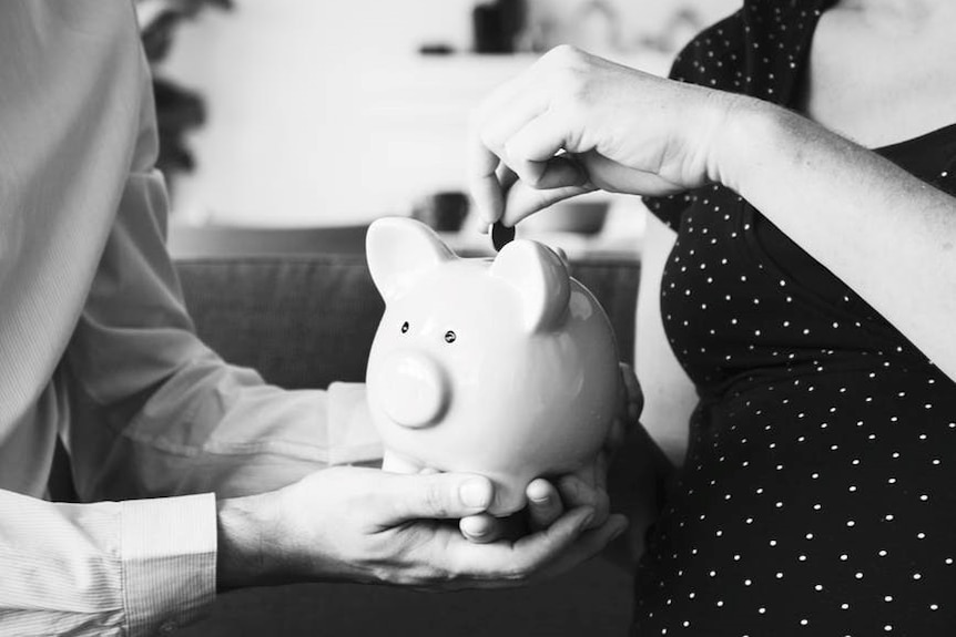 A woman deposits a coin into a piggy bank being held by a man.