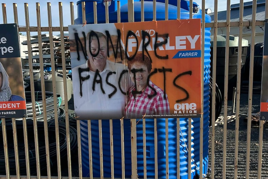 An orange One Nation poster with graffiti reading No more facists scrawled over it attached to a fence