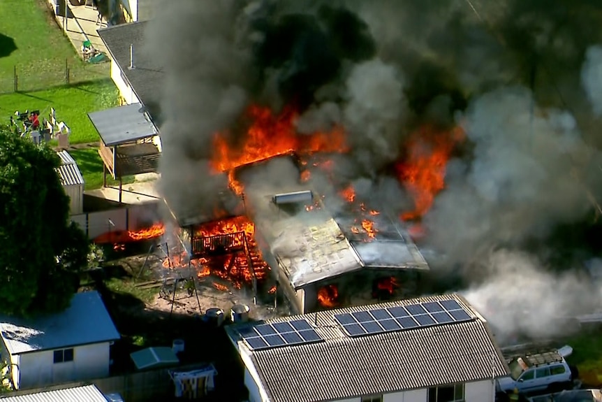 A veiew from above showing bright orange flames as smoke surrounding a house.